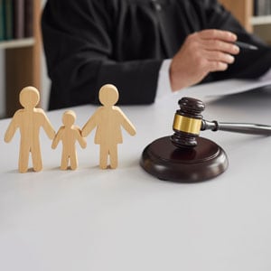 Lawyer in front of judge's table with gavel and wooden family, symbolizing a child custody order.