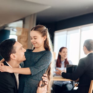 A father embraces his young daughter while meeting with lawyers, symbolizing the emotional challenges of custody battles